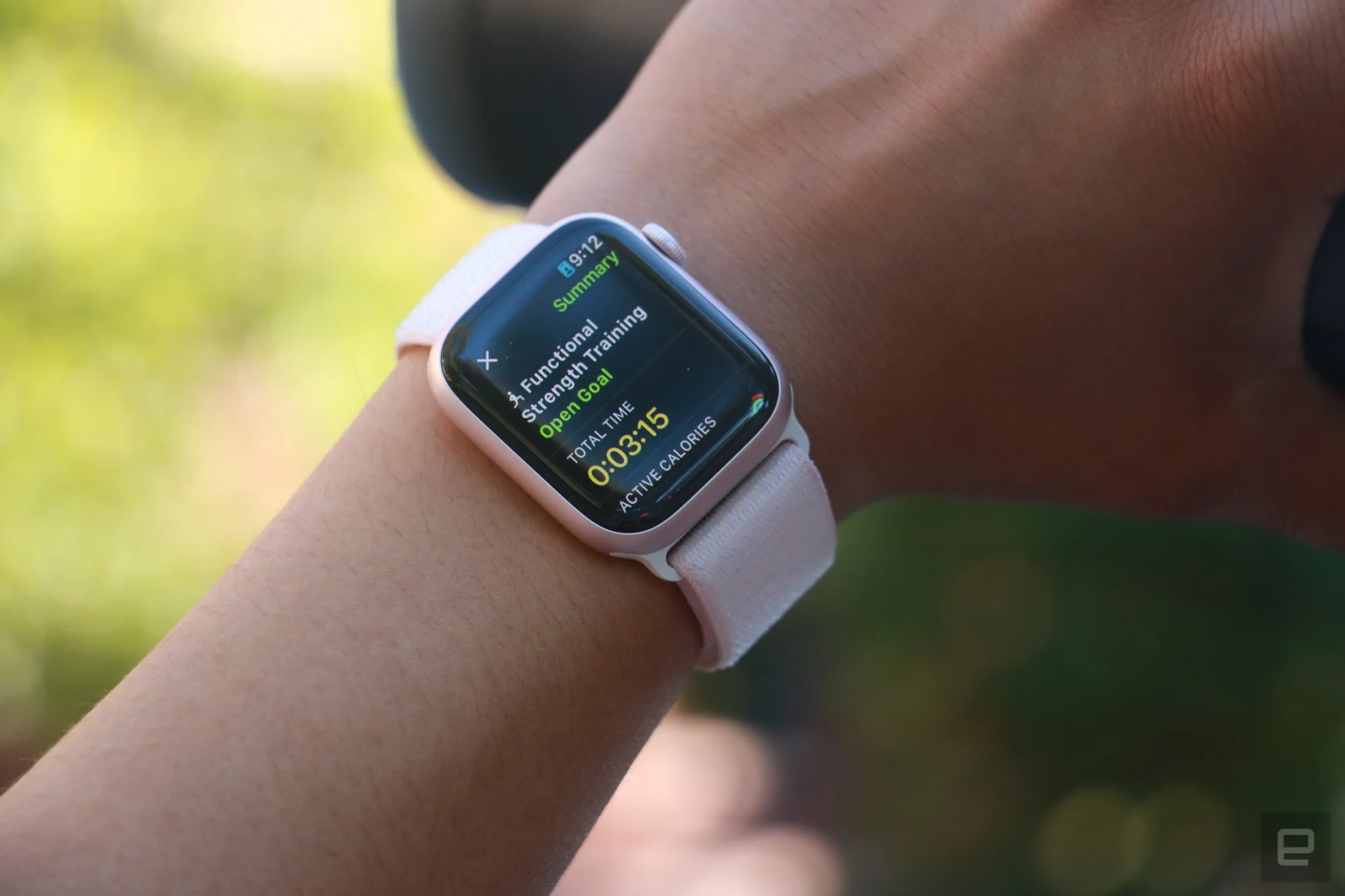 The Apple Watch Series 9 on a person's wrist, with the hand holding a black water bottle in the background. The screen shows the summary of a Functional Strength Training workout.