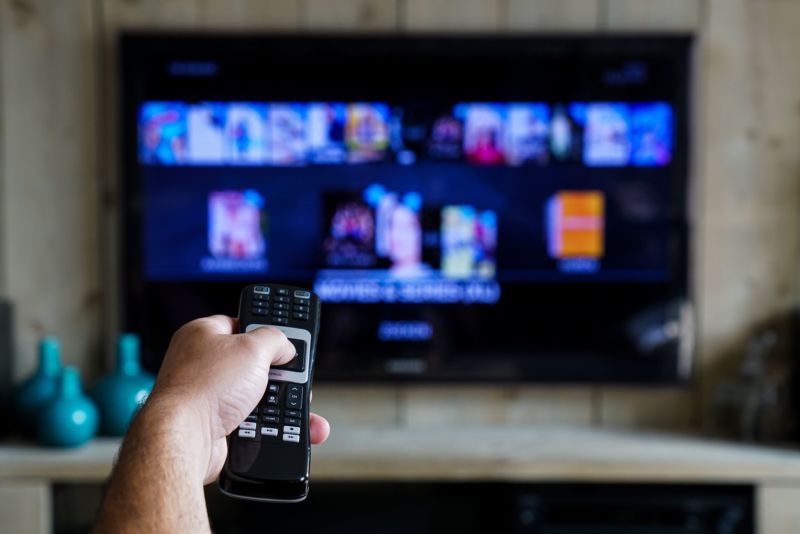 A person's hand pointing a TV remote at a TV.