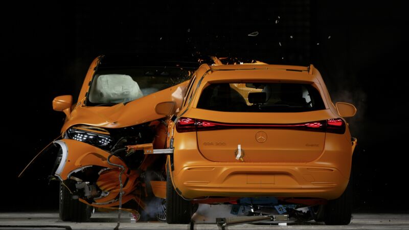 Two orange-painted Mercedes cars crash into each other head-on, seen from head-on.